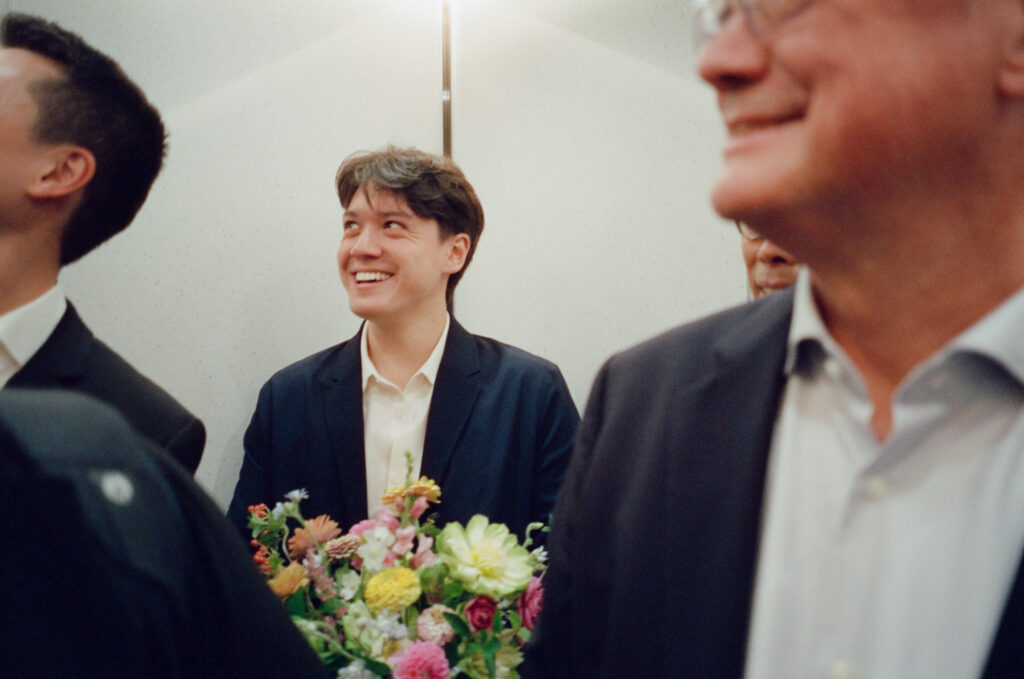 The groom's brother holds onto the groom's bouquet crafted by Roxy in the elevator among family in Boston City Hall.