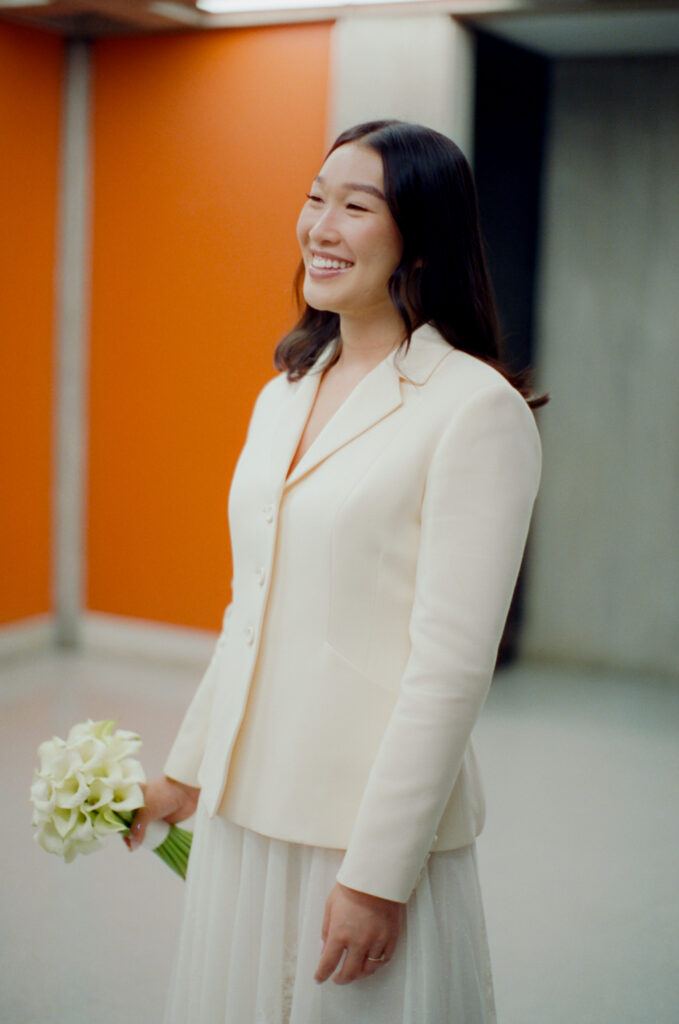Portrait of the bride in her white suit and skirt holding her bouquet of Calla Lillies and smiling at her Boston City Hall elopement