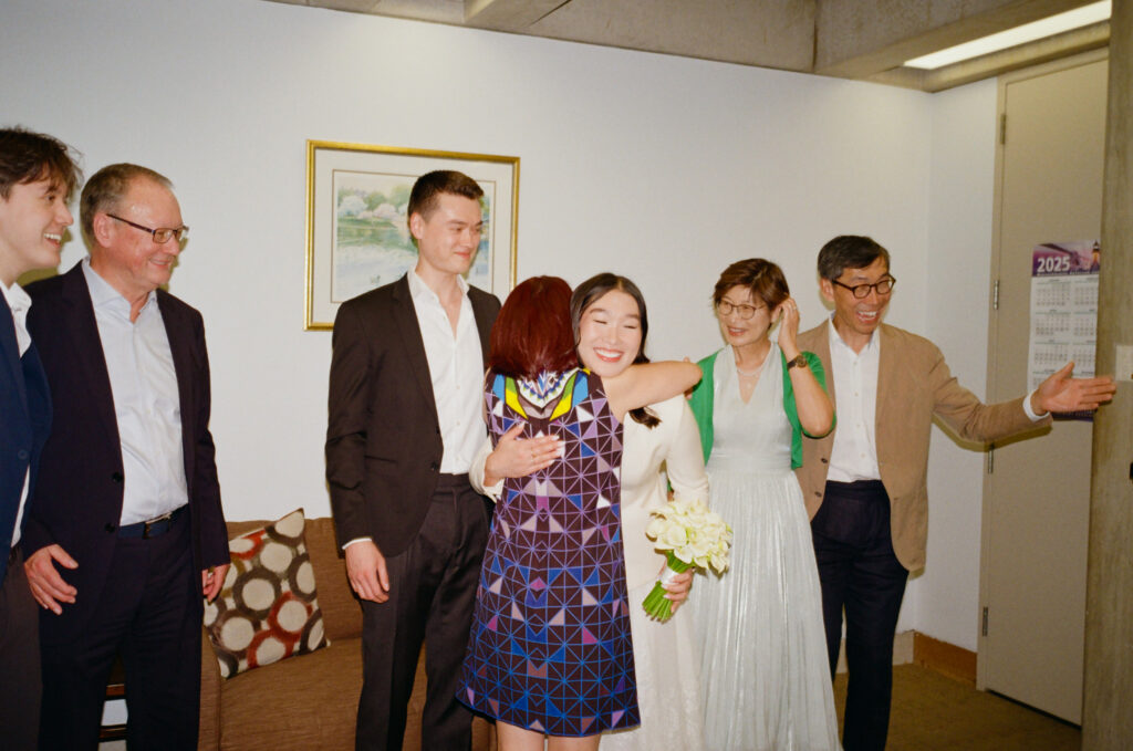 The bride and her mother-in-law exchange embraces around the groom and family as they finish their Boston City Hall elopement ceremony. 