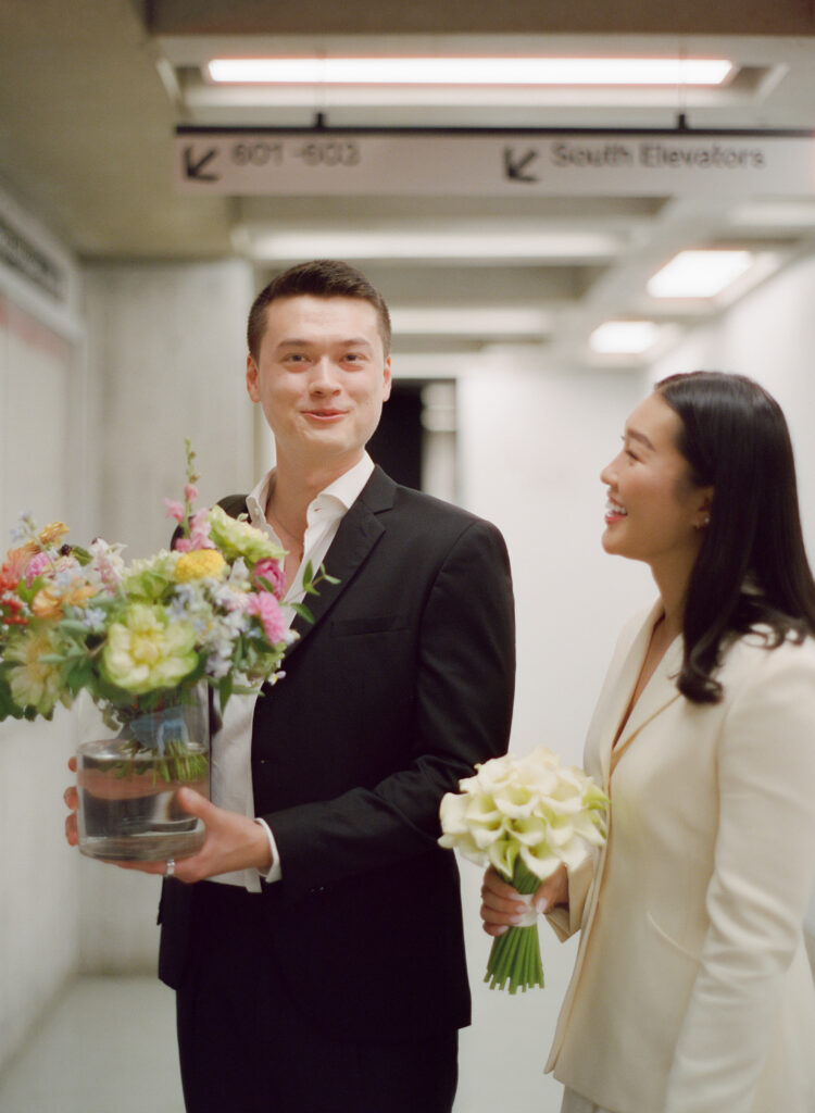 Candid of groom and bride holding their bouquets, gifted by Roxy and Wei Wei's mom, with smiles in Boston City Hall.