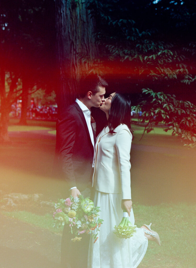 Profile photograph of bride and groom kissing, lush bouquets of white and pastel in hand, in Boston Public Garden -- film wedding photography.