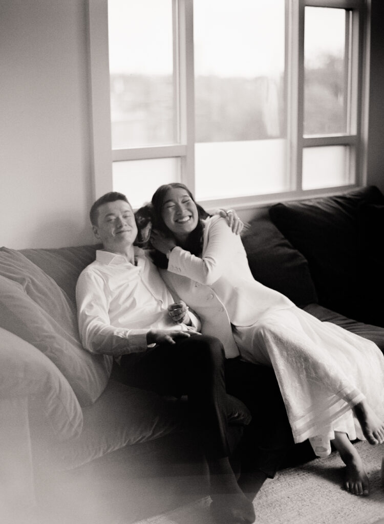 The bride and groom lay on each other with their dog on the couch in their living room after their Boston City Hall wedding elopement.