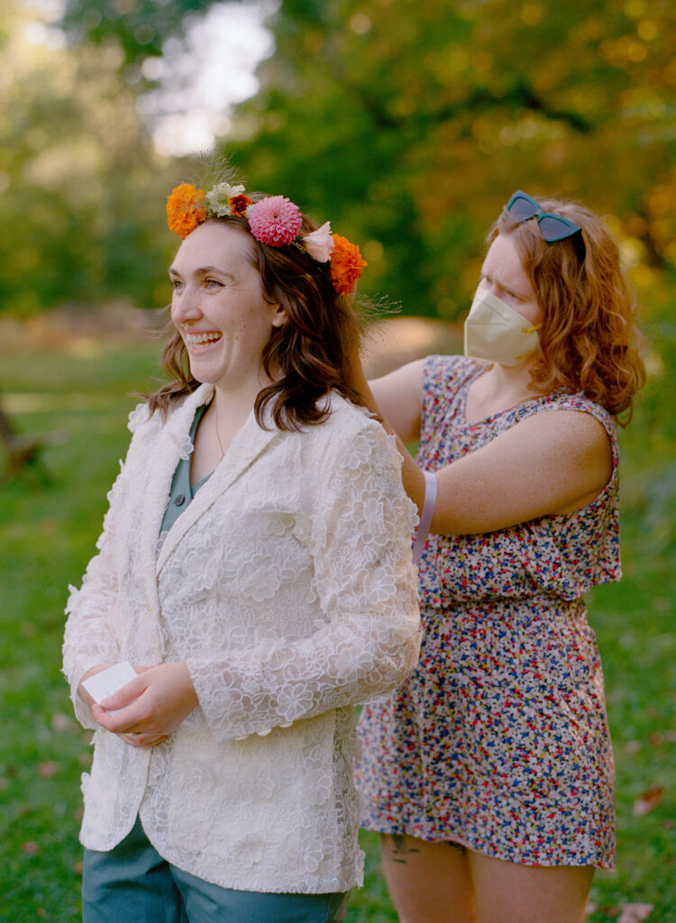 Woman on her elopement day smiles as a florist fixes her flower crown from behind. 