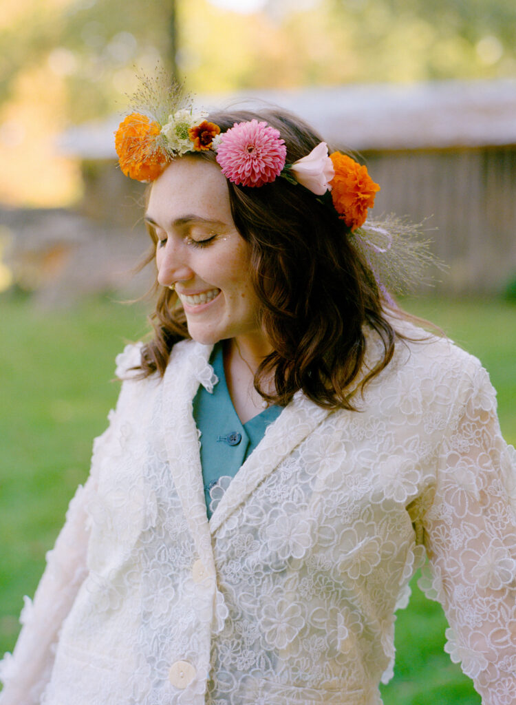 Portrait of woman on her elopement day. She looks down and away from the camera smiling. She wears a pink and orange flower crown, complimenting her white and green attire.