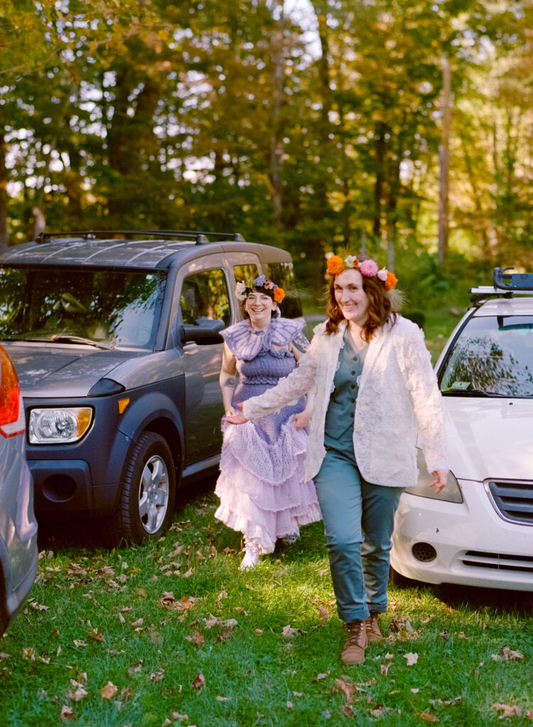A color film photograph of bride and bride walking from their cars in their full elopement-day attire, gleaming smiles on their faces