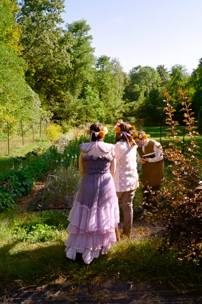 Couple stands in front of a flower garden for their elopement ceremony, with backs turned to the viewer.