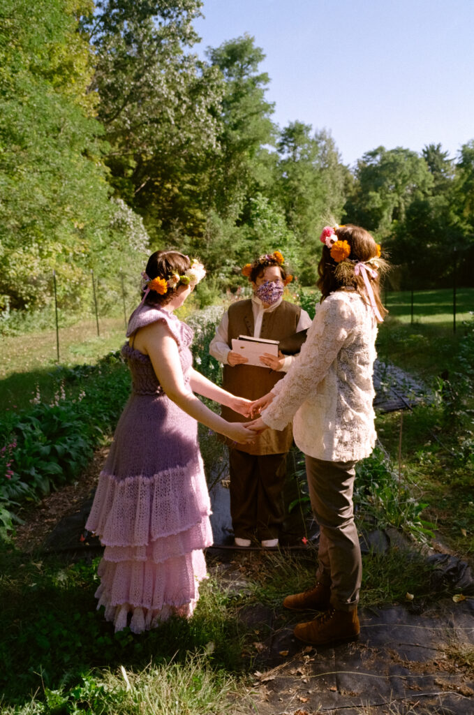 Color film photograph of a couple linking hands as they look towards their wedding officiant. 