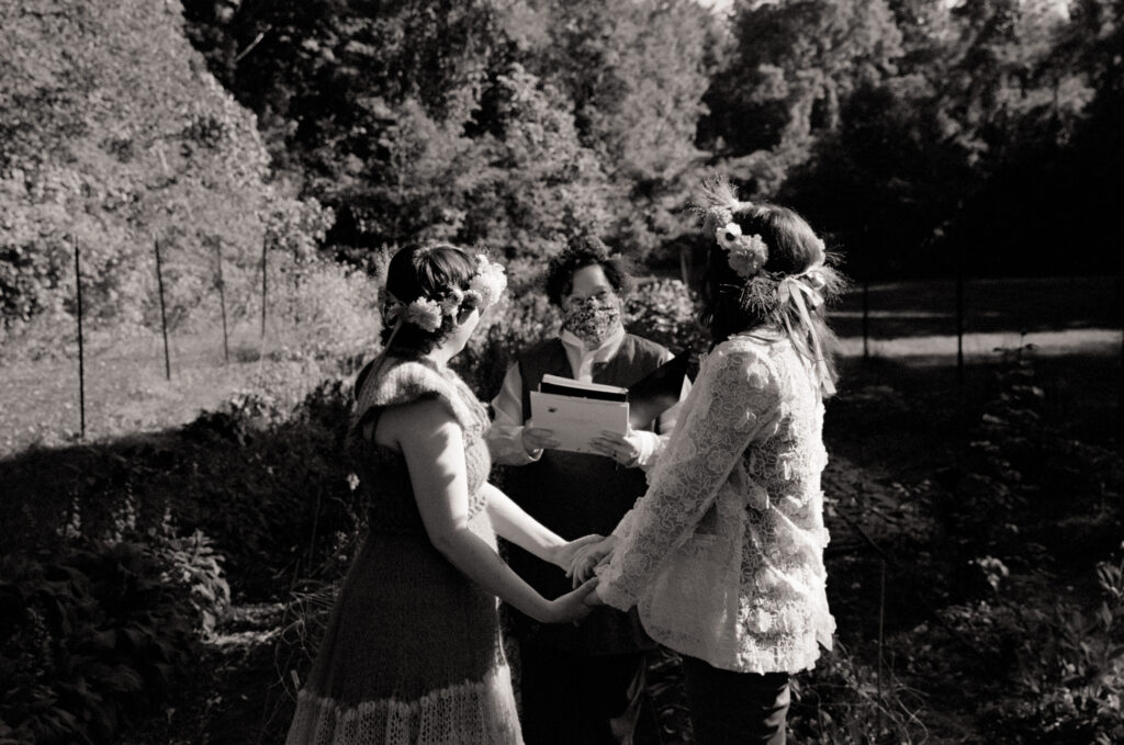 Black and white film photograph  of a couple holding hands and looking at their officiant at their wedding ceremony
