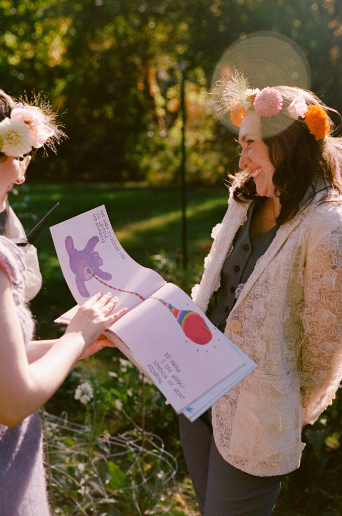 The bride in a suitcoat gleams as her partner flips the page of a picture book focused on love.