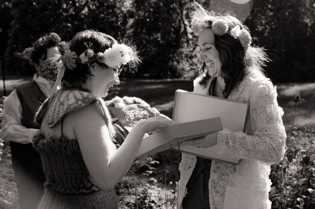 A black and white film photograph as romantic partners sift through a gift box at their wedding altar. 