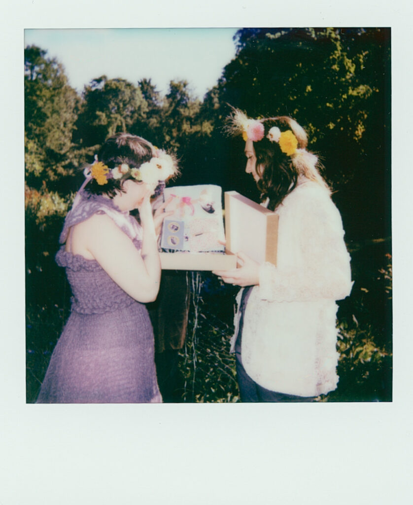 Polaroid photograph of brides opening a gift box at their wedding altar, revealing handmade gifts. 