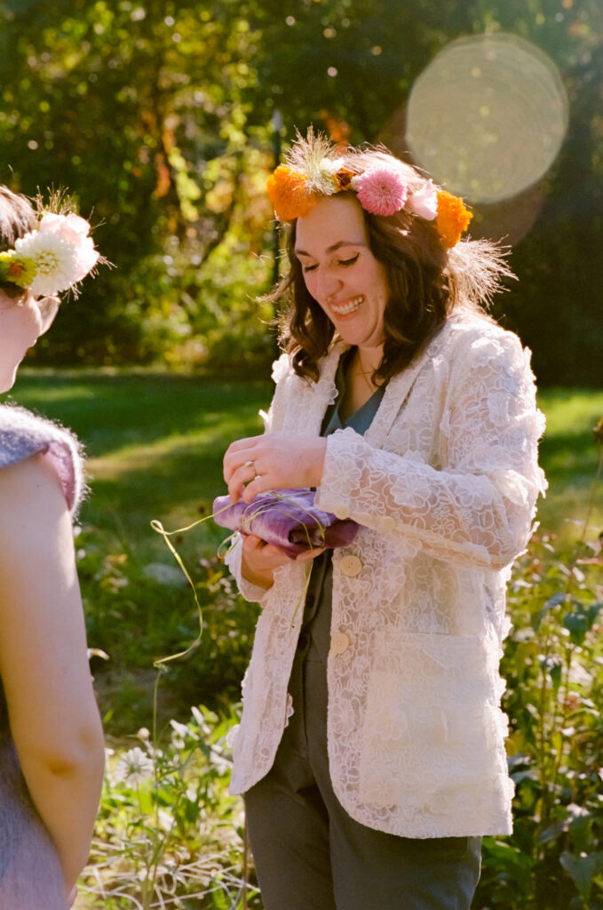 Bride in a lace suit and flower crown eagerly unravels their wedding day gift.
