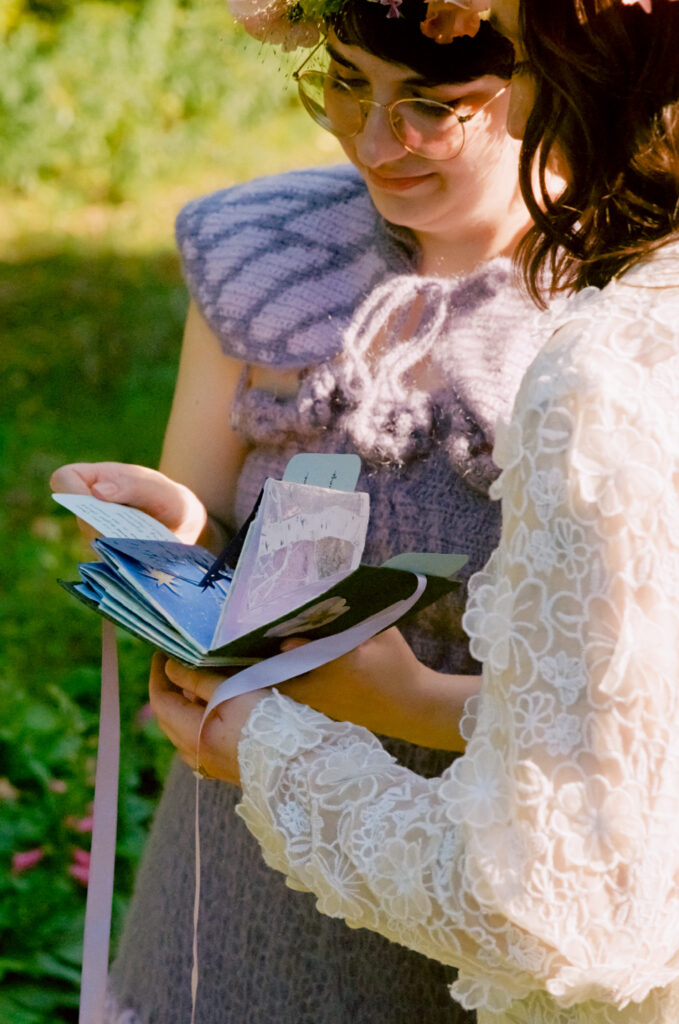 Brides hold their vow gift during the ceremony surrounded by lush green fields.