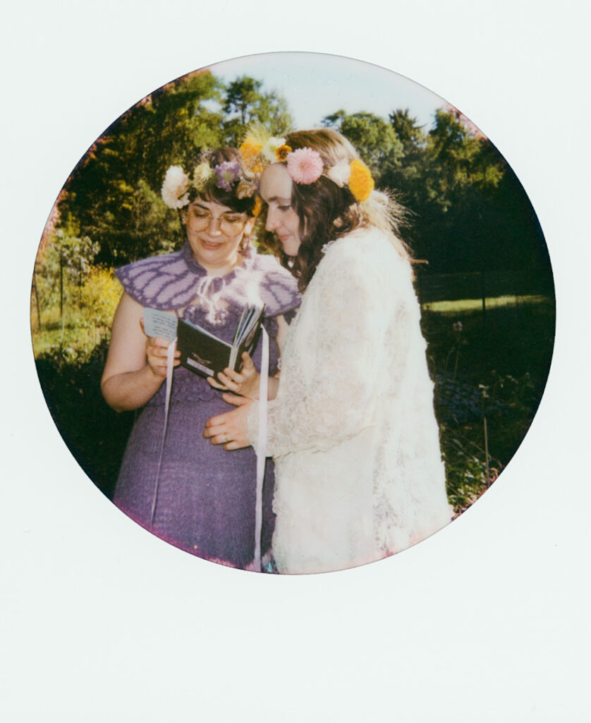 Color Polaroid Photograph of brides looking over a handwritten book together, backdropped by green forest.
