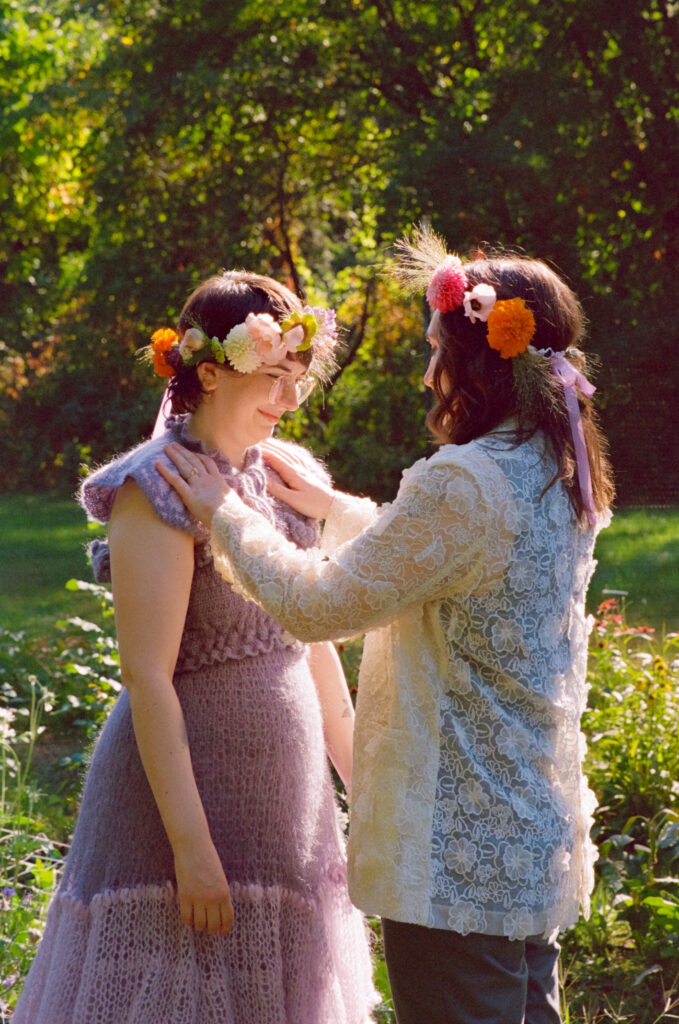 Bride adjusts her partners shawl during their wedding ceremony amongst a green field.