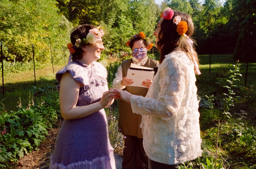 A couple links hands and smile at each other in front of their officiant at their wedding ceremony