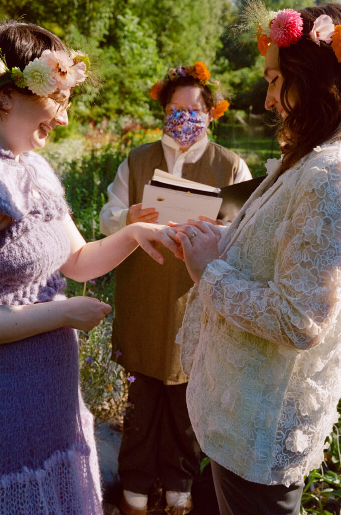 Bride slips on her partners ring in front of their officiant at their nature-themed wedding ceremony 