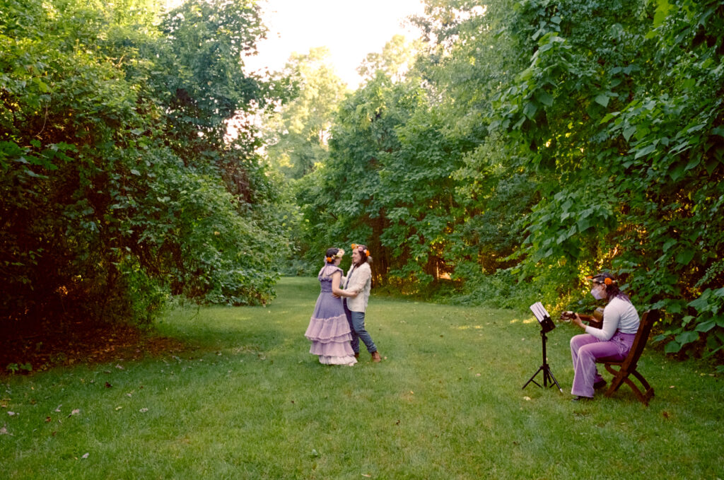 Color film wide angle shot of couple dancing their first dance alongside their guitarist at their wedding ceremony