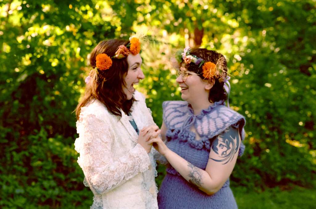 A married couples holds hands and face each other with bright smiles against a gorgeous forest background.