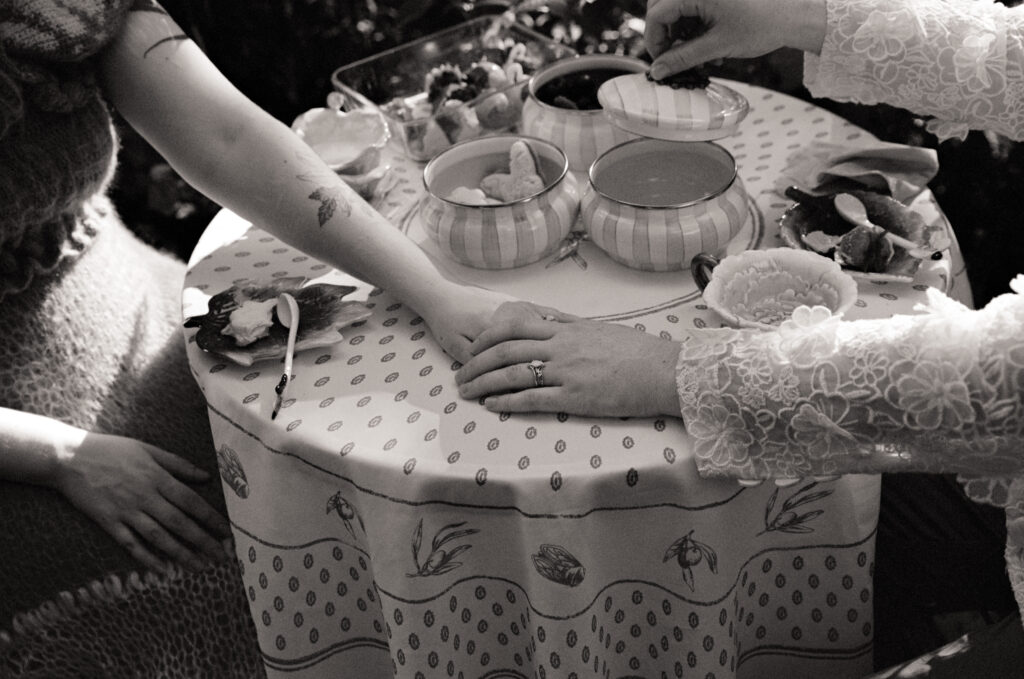 Close-up detail photograph of newlywed couple holding hands across a tea table