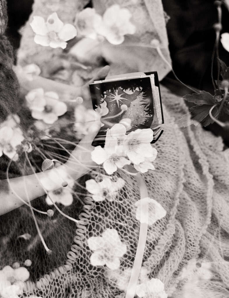 Black and white double exposure photograph of couple examining one of their personal wedding gifts, overlayed by flowers in bloom.