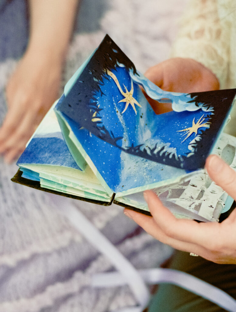 Close-up photograph of hand-made book, containing painted and paper-cut scenes, made by their partner as a newlywed gift.