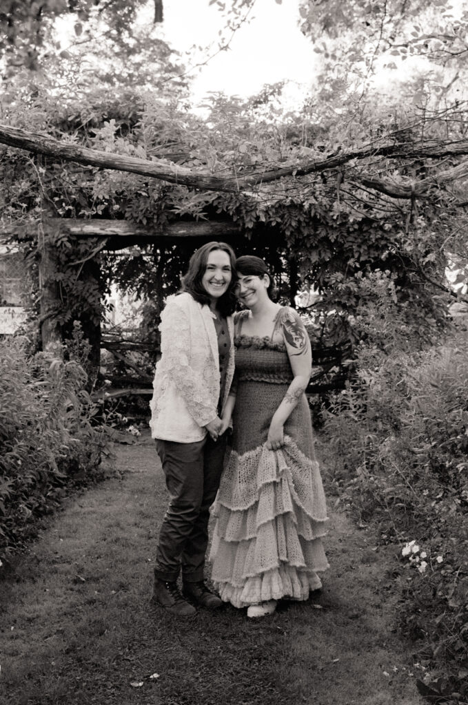 Full body portrait of couple on their wedding day, framed by a wooden archway.