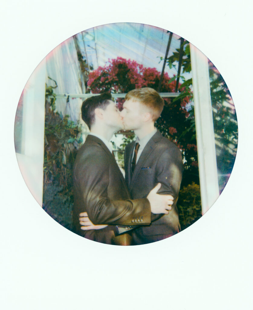 polaroid photo of queer couple kissing in green house