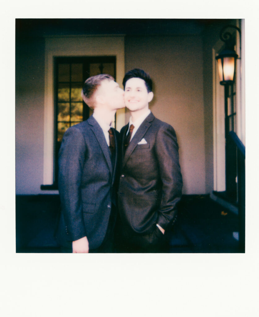 polaroid photo of a queer man kissing his husband on the cheek and smiling