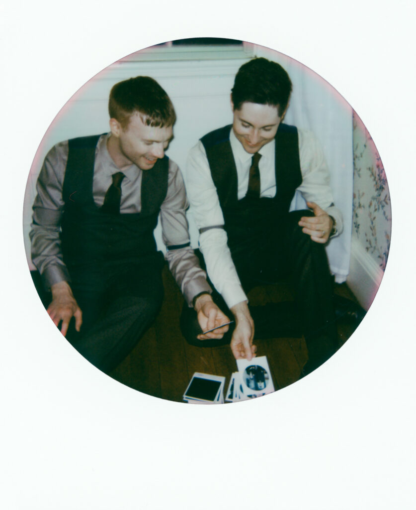 queer grooms looking at polaroid pictures while sitting on the floor in a polaroid photo