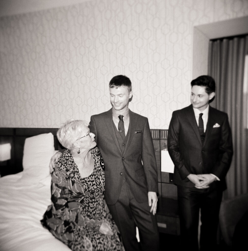 black and white photo of queer couple smiling and looking down at a older women