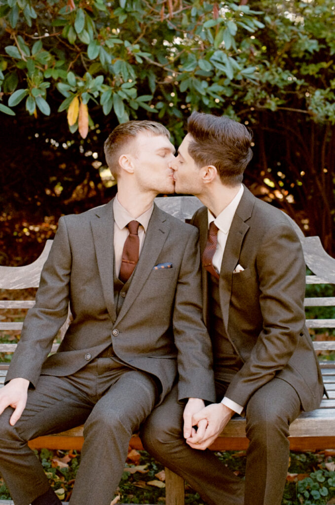 Queer couple sitting on bench while holding hands and kissing