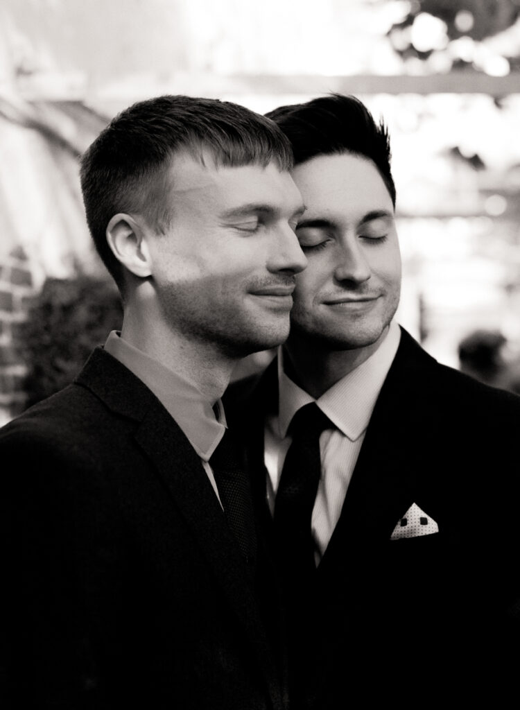 Black and white photo of queer couple with their eyes closed and cheeks touching