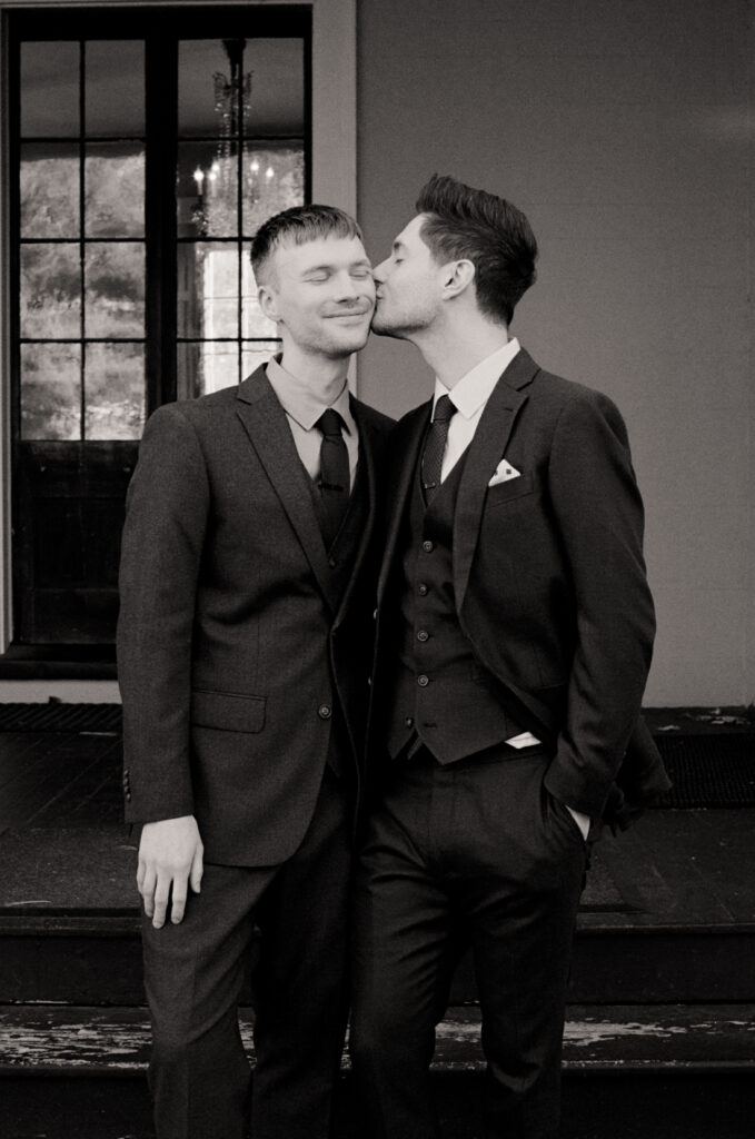 black and white photo of two queer men posing and kissing on the cheek at the Lyman Estate on their wedding day