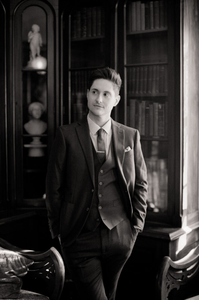 black and white photo of a queer man posing in front of a library on his wedding day