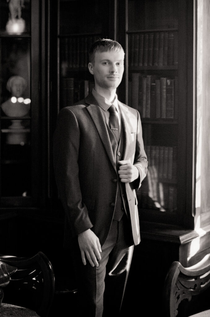 black and white photo of a queer man posing in front of a library on his wedding day