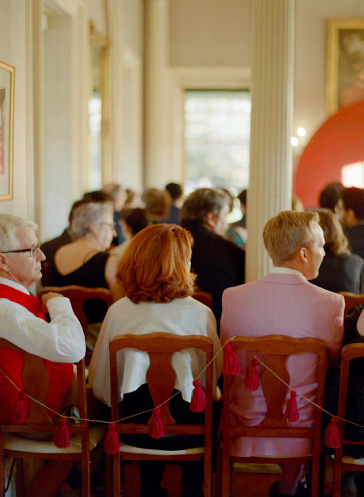 back of wedding guests sitting in wooden chairs