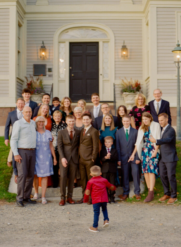 family posing and smiling at little boy running towards them in candid photo