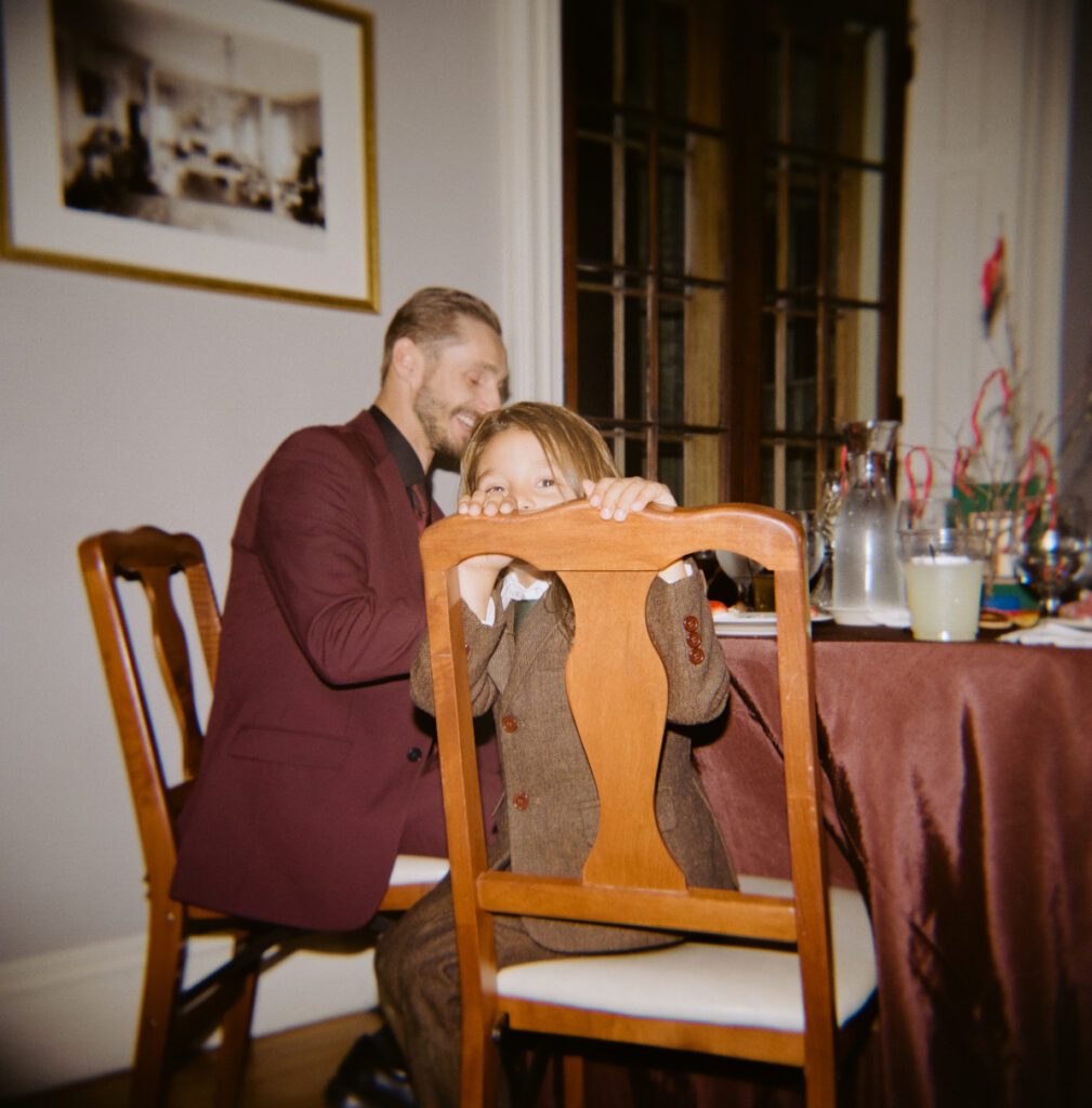 child and father sitting at table while son looks into the camera