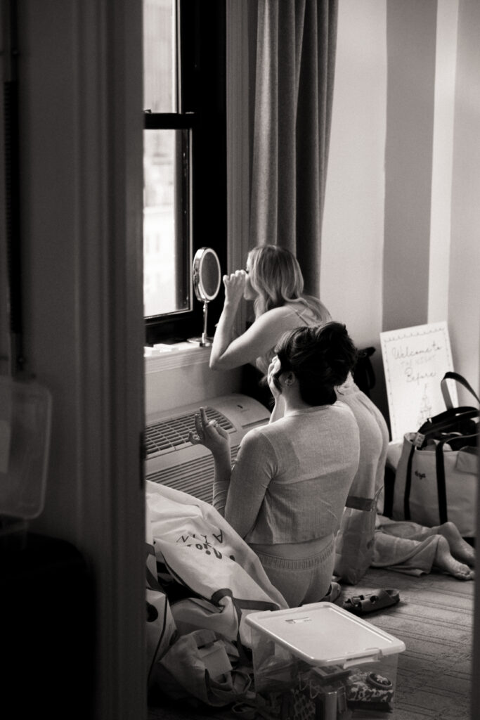 bridesmaids sitting on the floor looking at a mirror getting ready before the wedding on black and white film photos