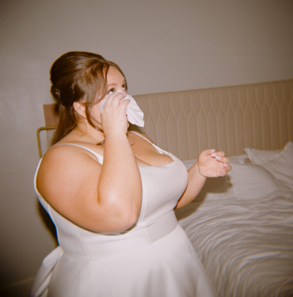 bride in wedding dress wiping her face with a tissue