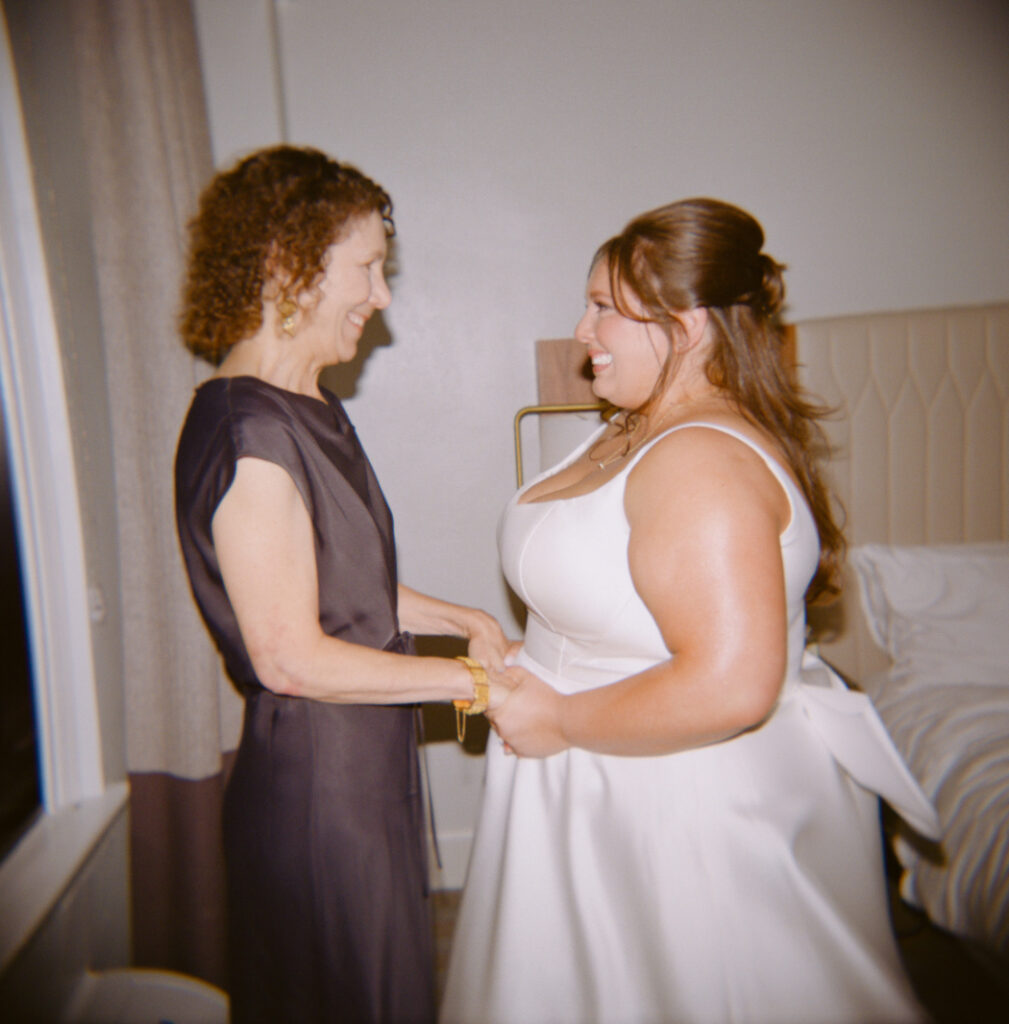bride in wedding dress holding hands and smiling at her mother figure