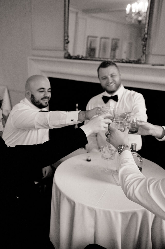 black and white film photo of groom and groomsmen sitting at a table having a drink