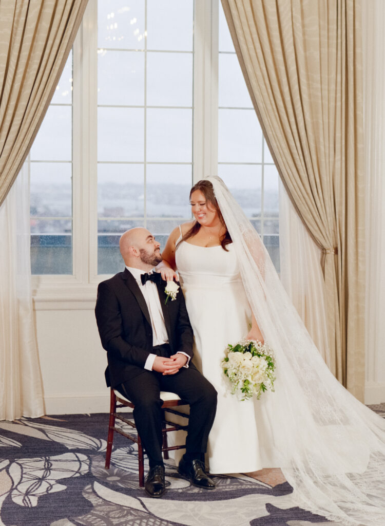bride and groom smiling at each other in front of windows