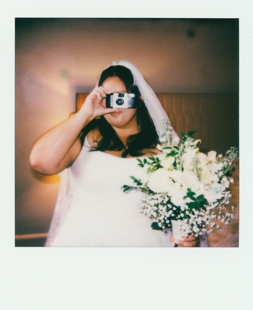 polaroid photograph of bride in a wedding dress holding a camera and a bouquet of flowers