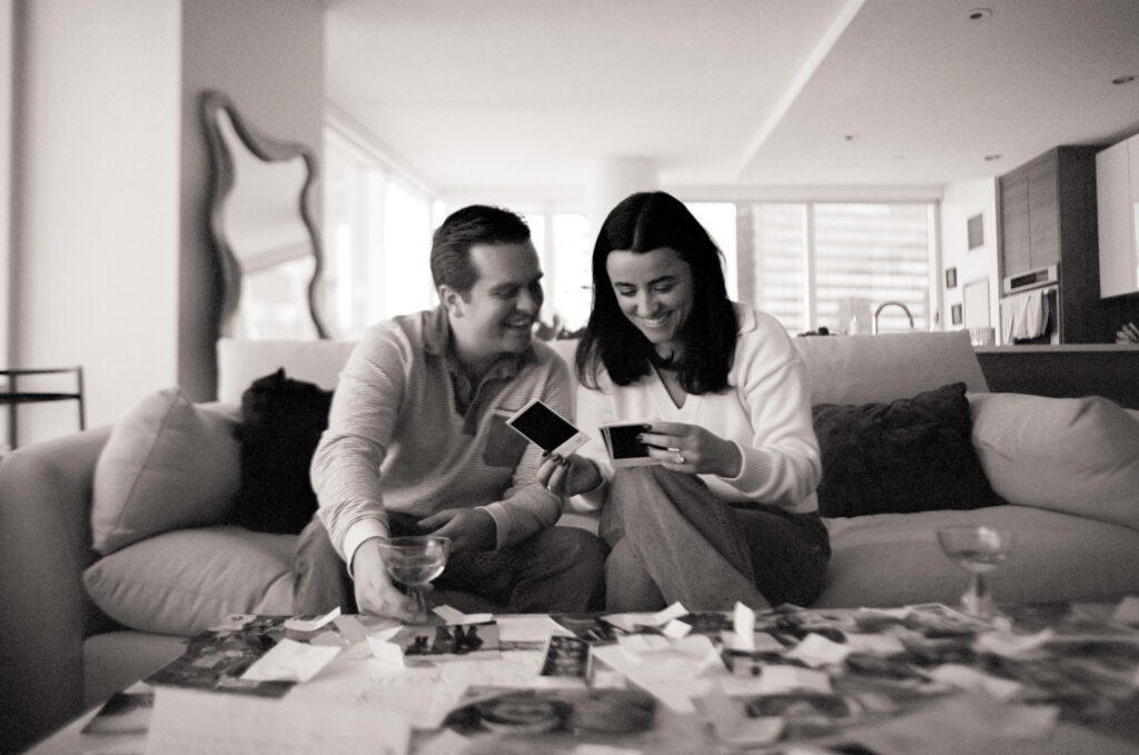 a man and woman sitting on a couch looking at photos at a engagement shoot on film 