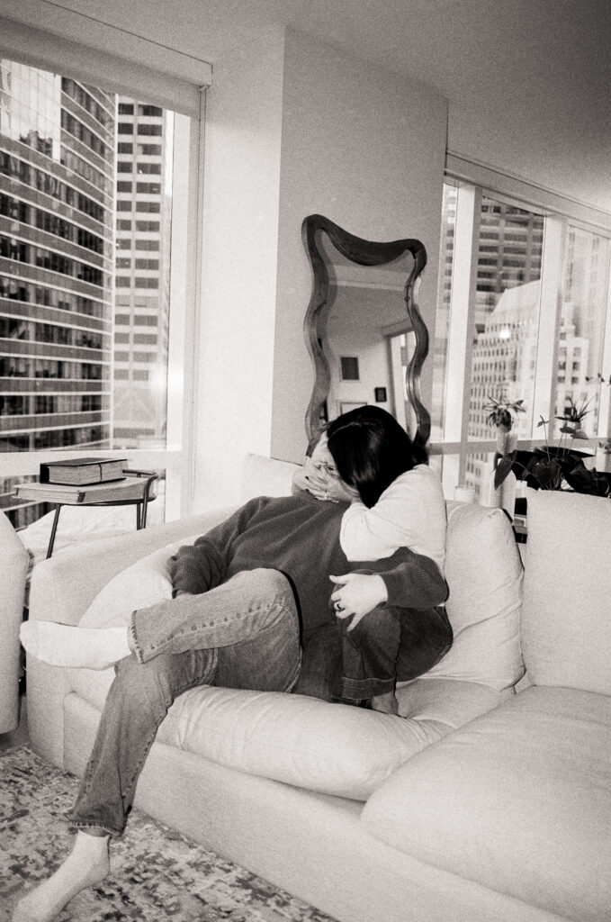 couple sitting on couch kissing and hugging in black and white photo during a film engagement photo 