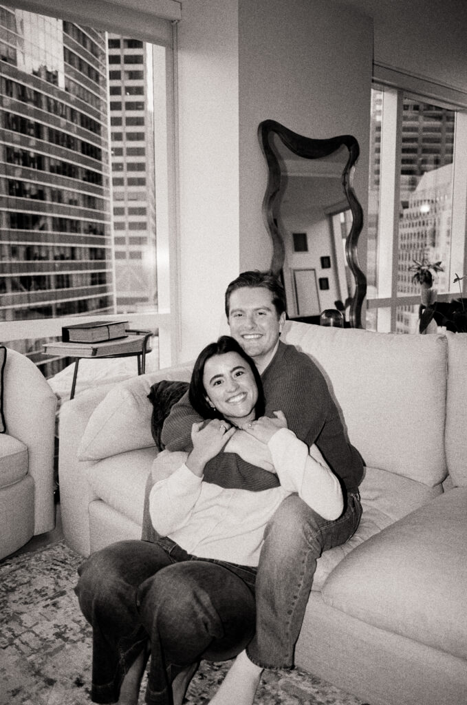 couple sitting on the couch and smiling in black and white photo during film engagement photos 