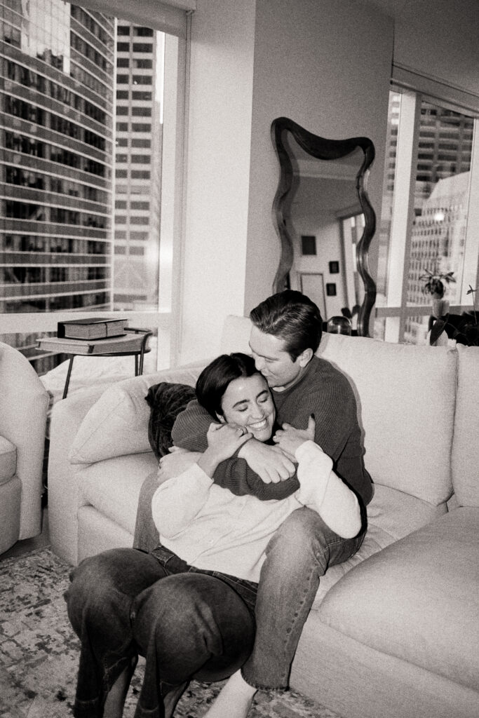 couple sitting on the couch and smiling in black and white photo during film engagement photos 