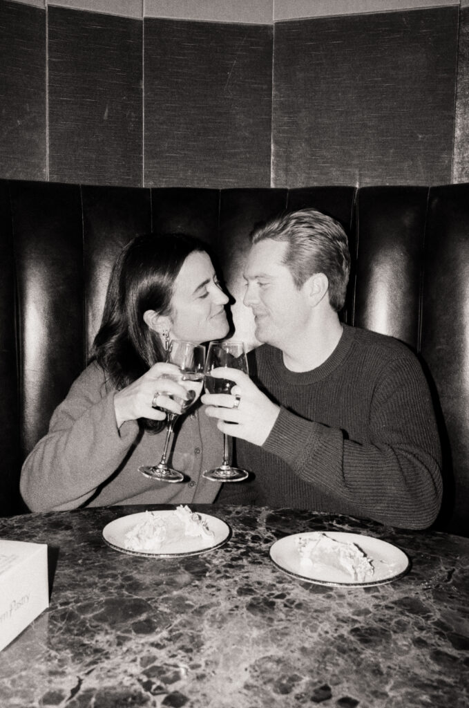 couple cheers wine glasses in a restaurant booth with a slice of cake  